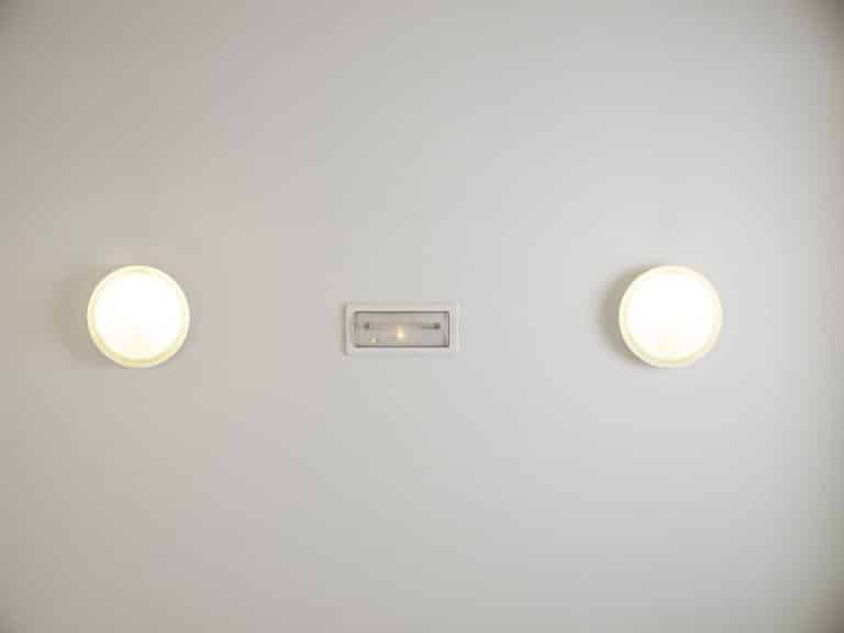 Two round wall lights beside a small emergency light unit on a white wall