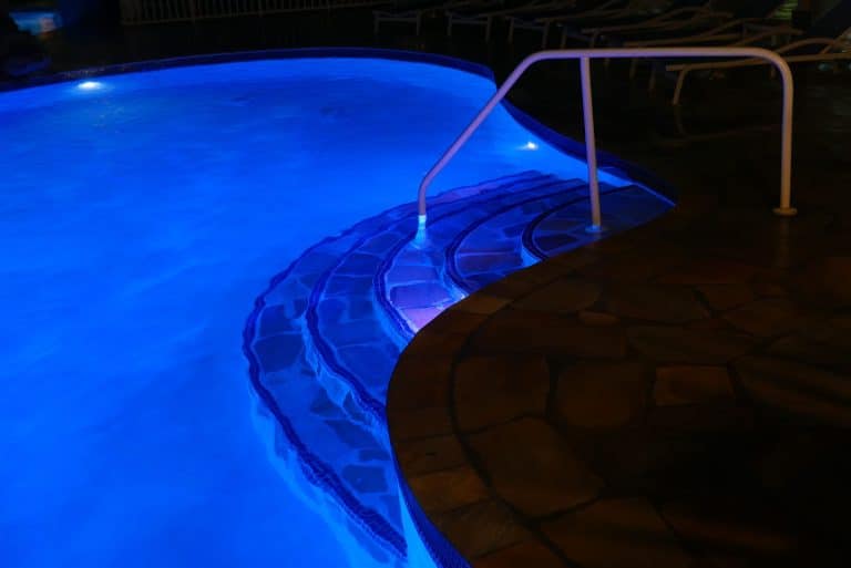 Backyard swimming pool glowing blue from underwater lights at night